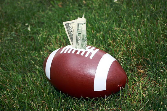 Football and One Hundred Dollar Bill on a Green Lawn